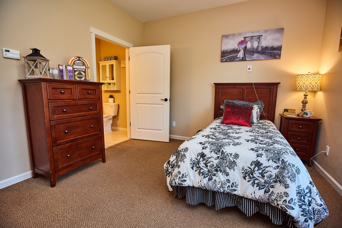 A cozy bedroom with a single bed, featuring decorative pillows and wall art, adjacent to an open bathroom door.
