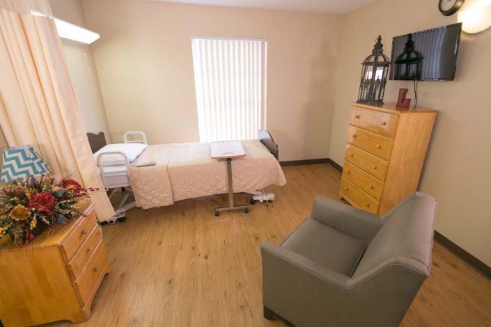 A small room with a hospital bed, armchair, and wooden furniture.
