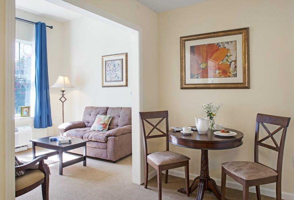 A cozy living and dining area with a sofa, round table, chairs, and artwork on the walls.