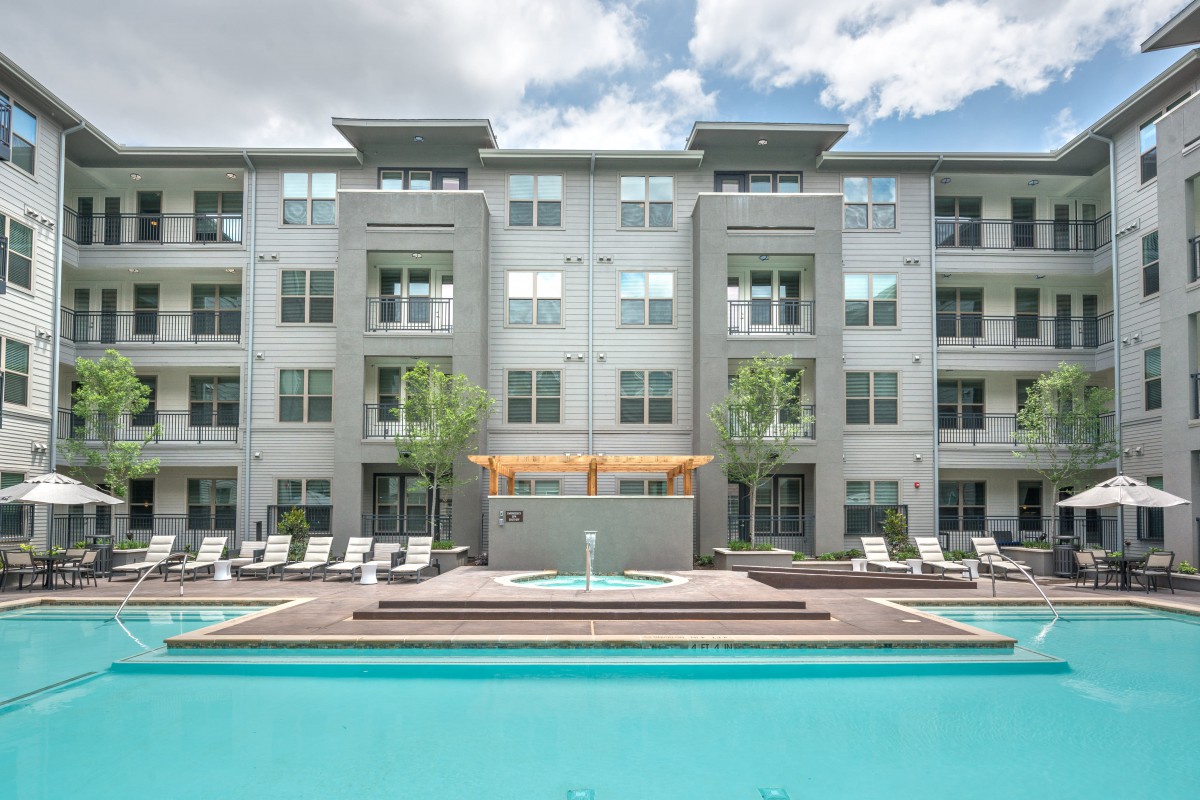 A modern apartment building with a pool in the foreground, showcasing urban residential living.