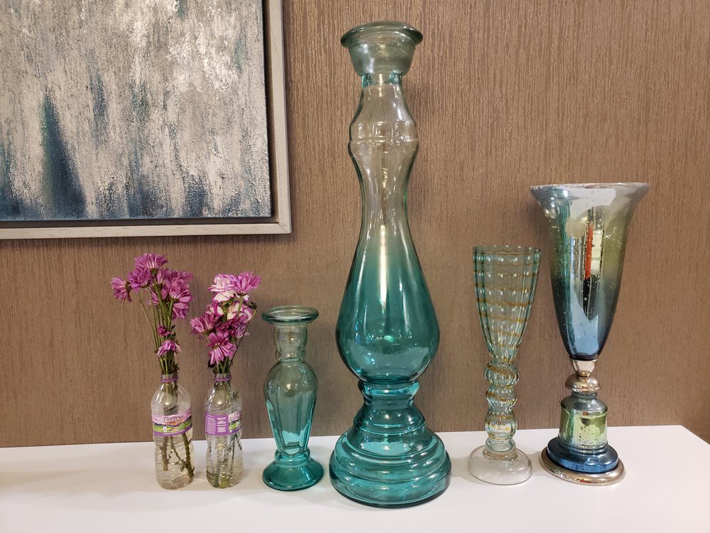 A collection of colorful glass vases with pink flowers displayed on a white surface, set against a neutral background.