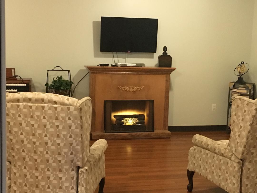 A cozy living room with a fireplace, TV mounted above, and patterned chairs.