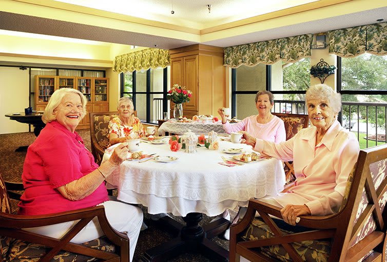 A group of senior women enjoying a tea party at a dining table indoors.