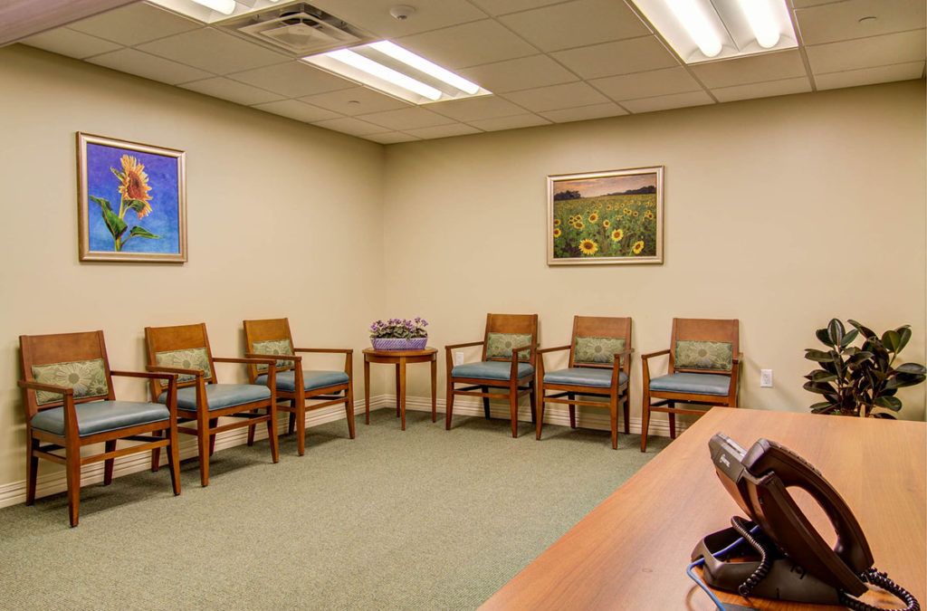 A small waiting room with chairs arranged along the walls and artwork displayed on the walls.