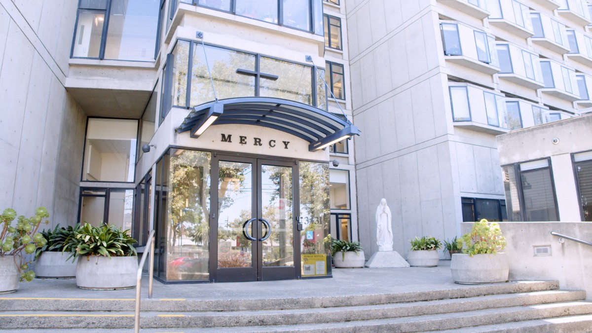 Entrance of a modern building with glass doors and a statue beside it.