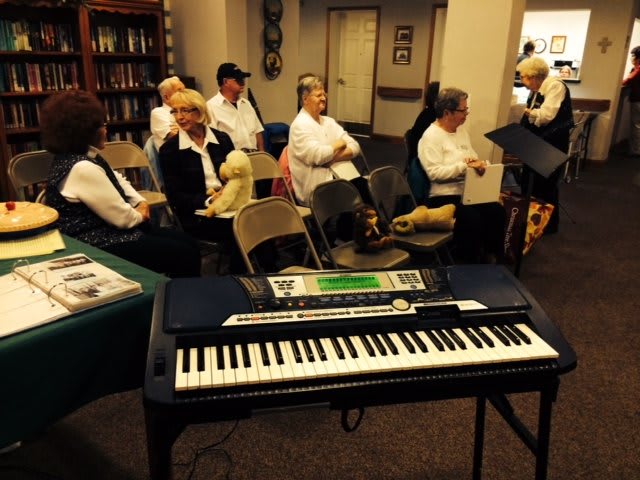 A group of adults sitting and preparing for a musical performance with a keyboard in the foreground.