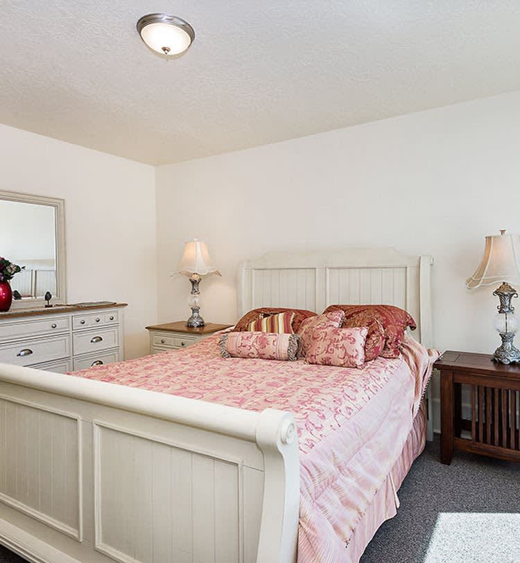 A cozy bedroom featuring a bed with a patterned quilt, flanked by nightstands and decorated with lamps, alongside a dresser with a mirror.