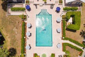 Aerial view of a swimming pool surrounded by lounge chairs and umbrellas in a landscaped patio area.