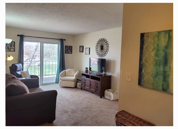 Cozy living room with a sofa, chair, and TV, featuring artwork and a large window for natural light.