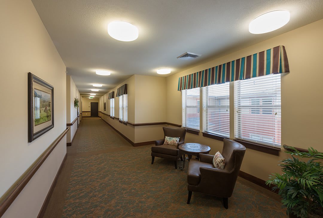 A well-lit hallway with chairs and a small table by the windows.
