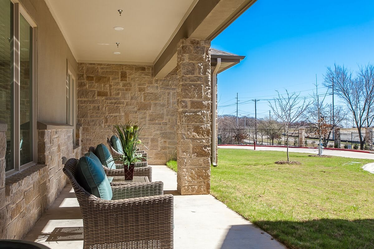 A sunny outdoor patio with wicker chairs and a brick wall overlooking a green lawn.