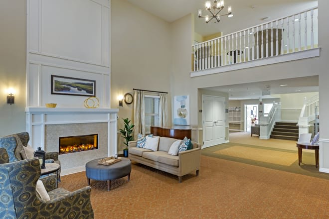 A spacious living room with a modern fireplace, plush sofa, and elegant chandelier under a high ceiling.