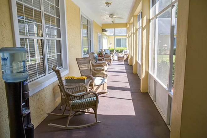 A bright porch with several rocking chairs and large windows letting in sunlight.