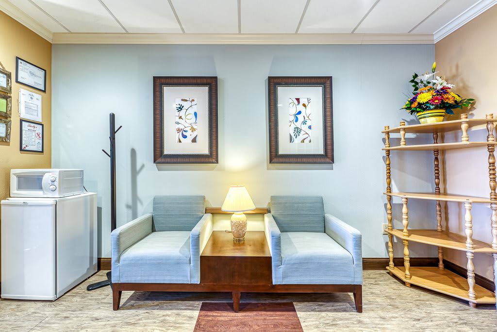 A cozy waiting room with two blue armchairs and a wooden table, adorned with framed artwork and a warm lamp.