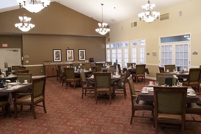 A spacious dining room with neatly arranged tables and chairs, illuminated by chandeliers.