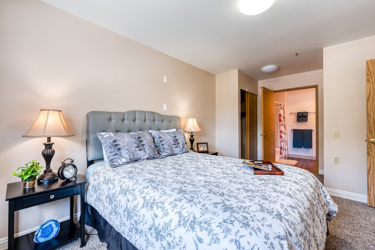 A cozy bedroom with a neatly made bed, bedside lamps, and light-colored walls.