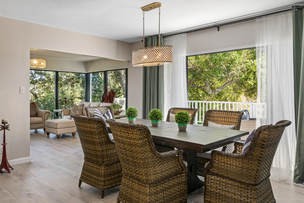 A modern dining room with wicker chairs and a wooden table, surrounded by large windows that let in natural light.