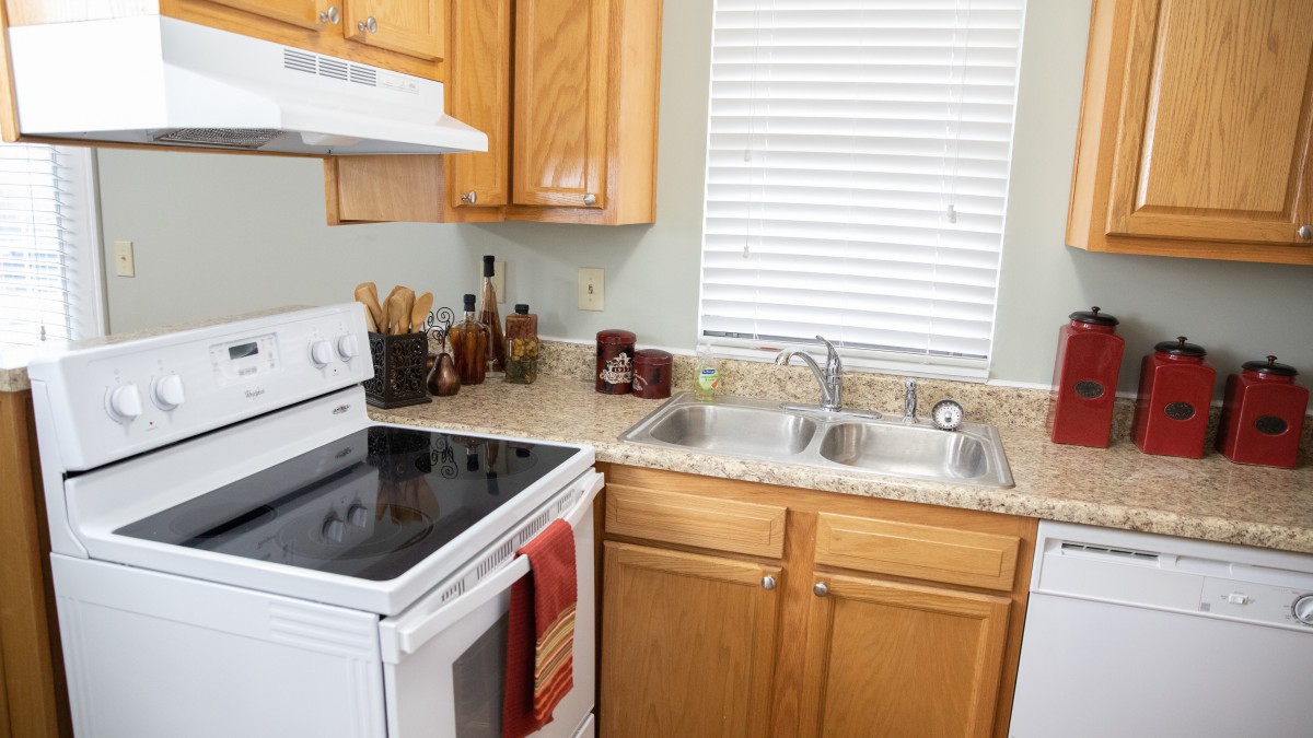 A cozy kitchen with wooden cabinets, a stove, a double sink, and various utensils on the countertop.