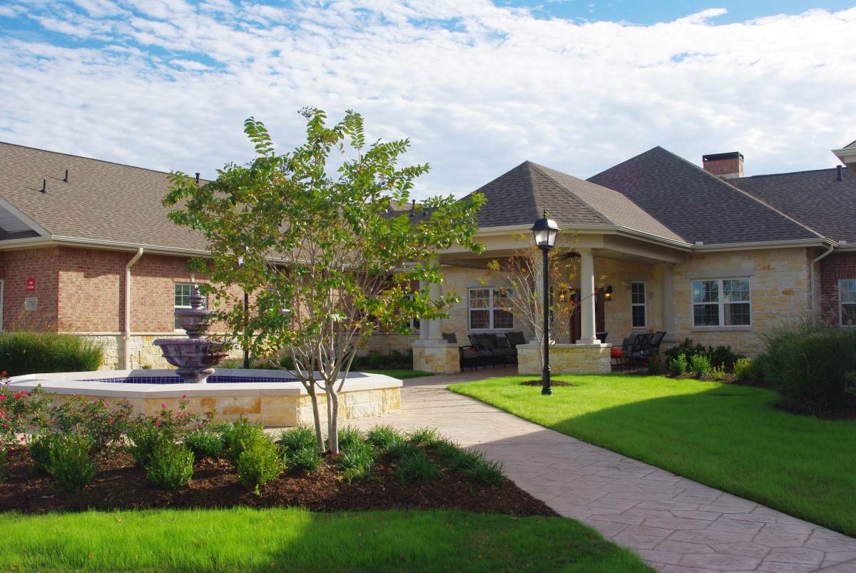 A well-maintained house with a manicured lawn and landscaping featuring a fountain and brick pathway.