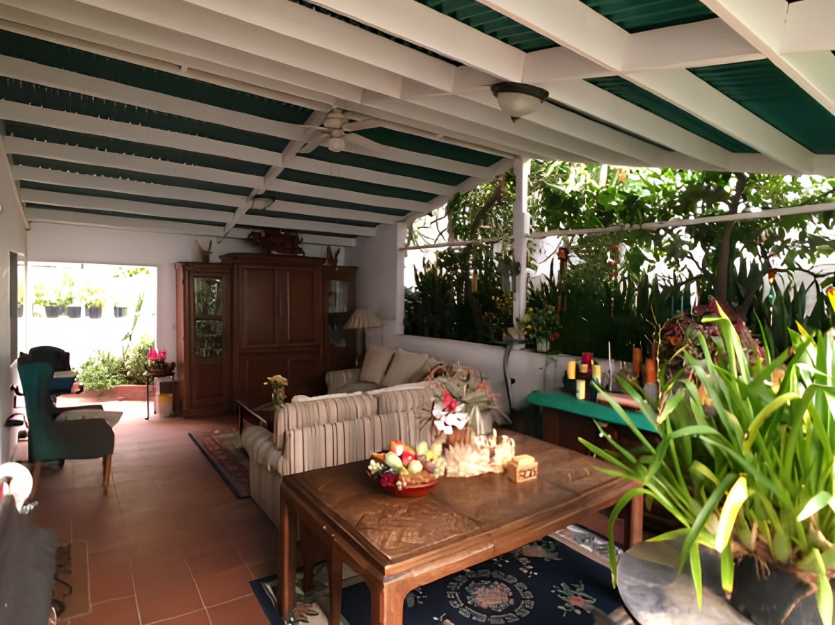 A cozy covered patio with a sofa, table, and decorative plants.