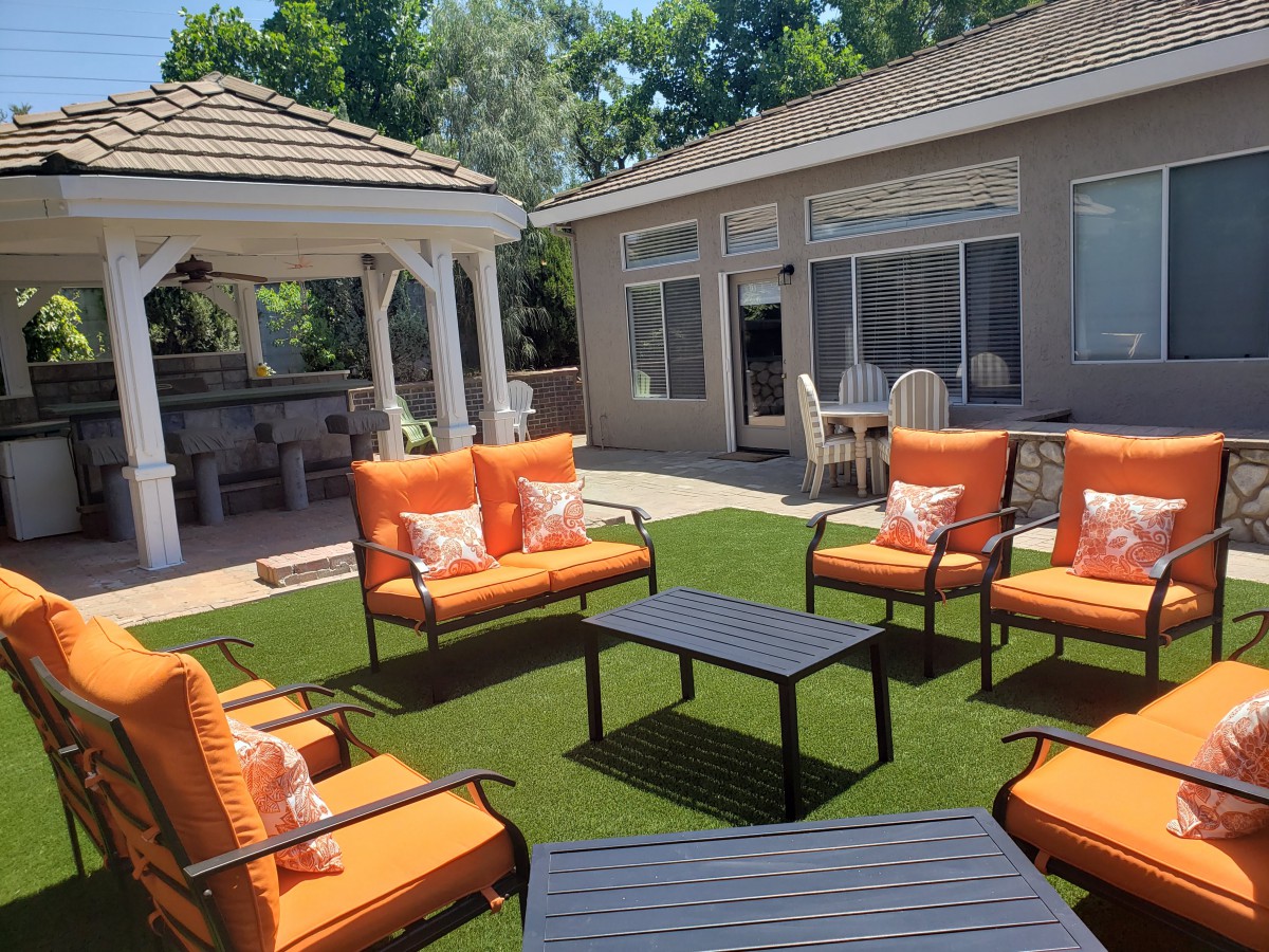 A cozy outdoor patio with orange-cushioned seating and a gazebo in the backyard.