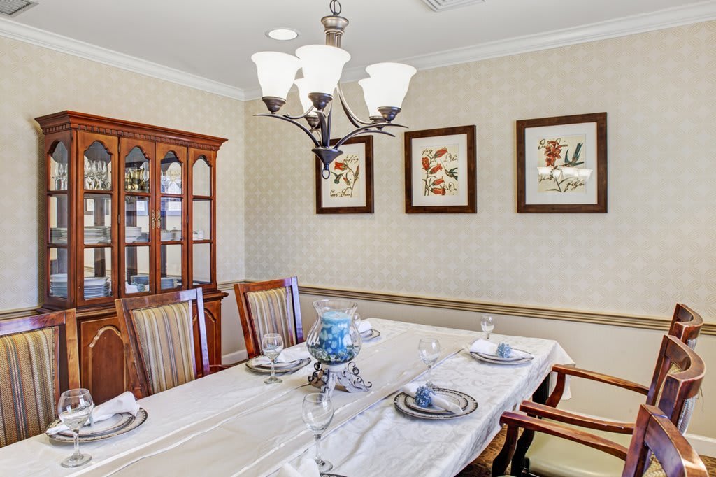 A cozy dining room with a set table, elegant chandelier, and decorative artwork on the walls.