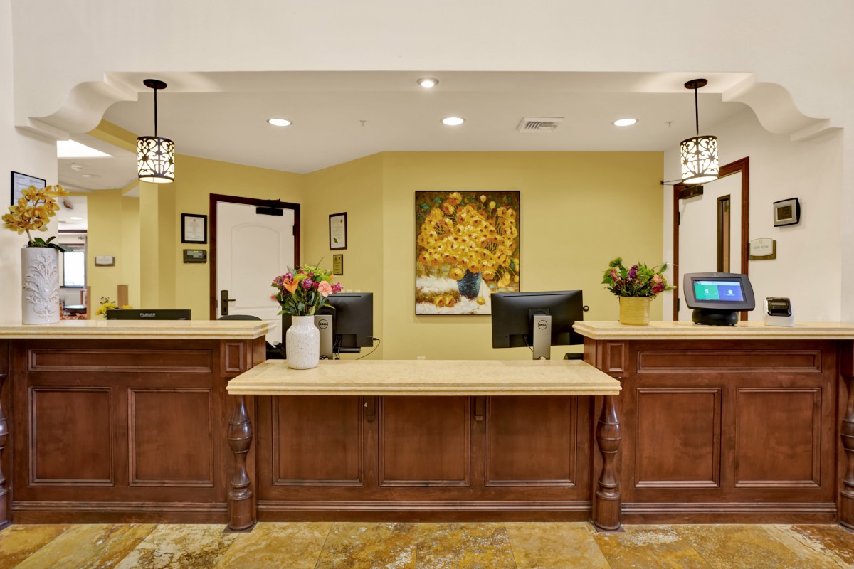 A well-lit reception desk with computers and decorative flowers in a lobby area.