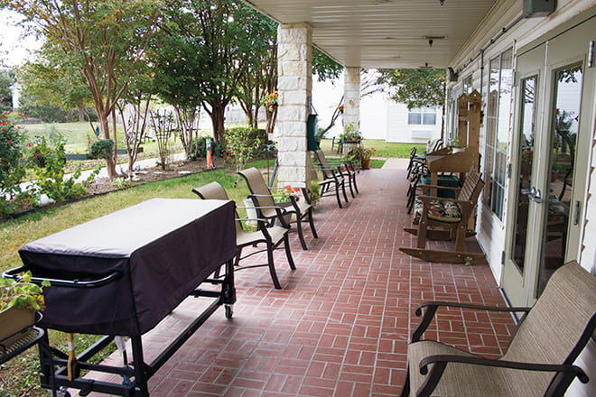 A covered porch with multiple chairs overlooking a garden space.