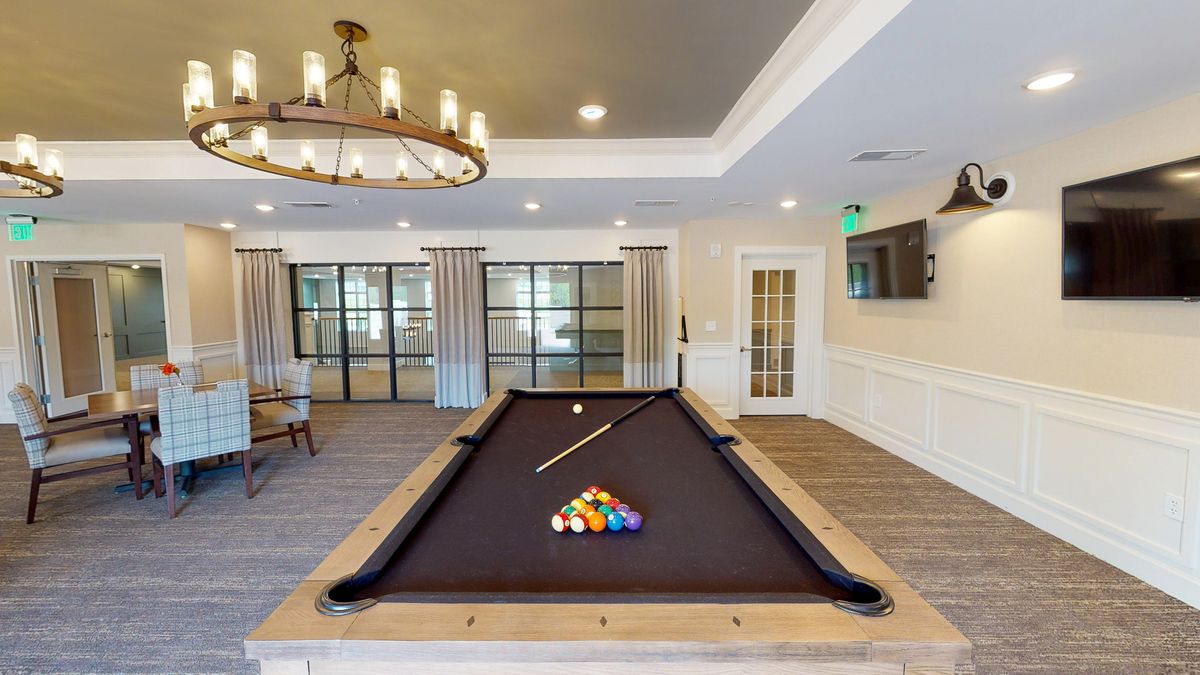 A stylish billiard room featuring a pool table under a chandelier with comfortable seating in the background.