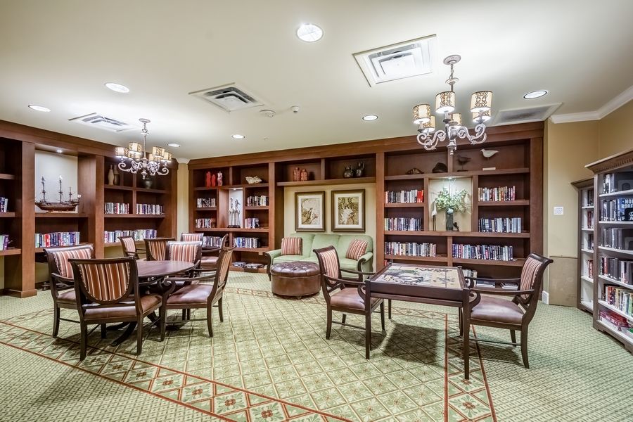A cozy library room with bookshelves, tables, and chandeliers.