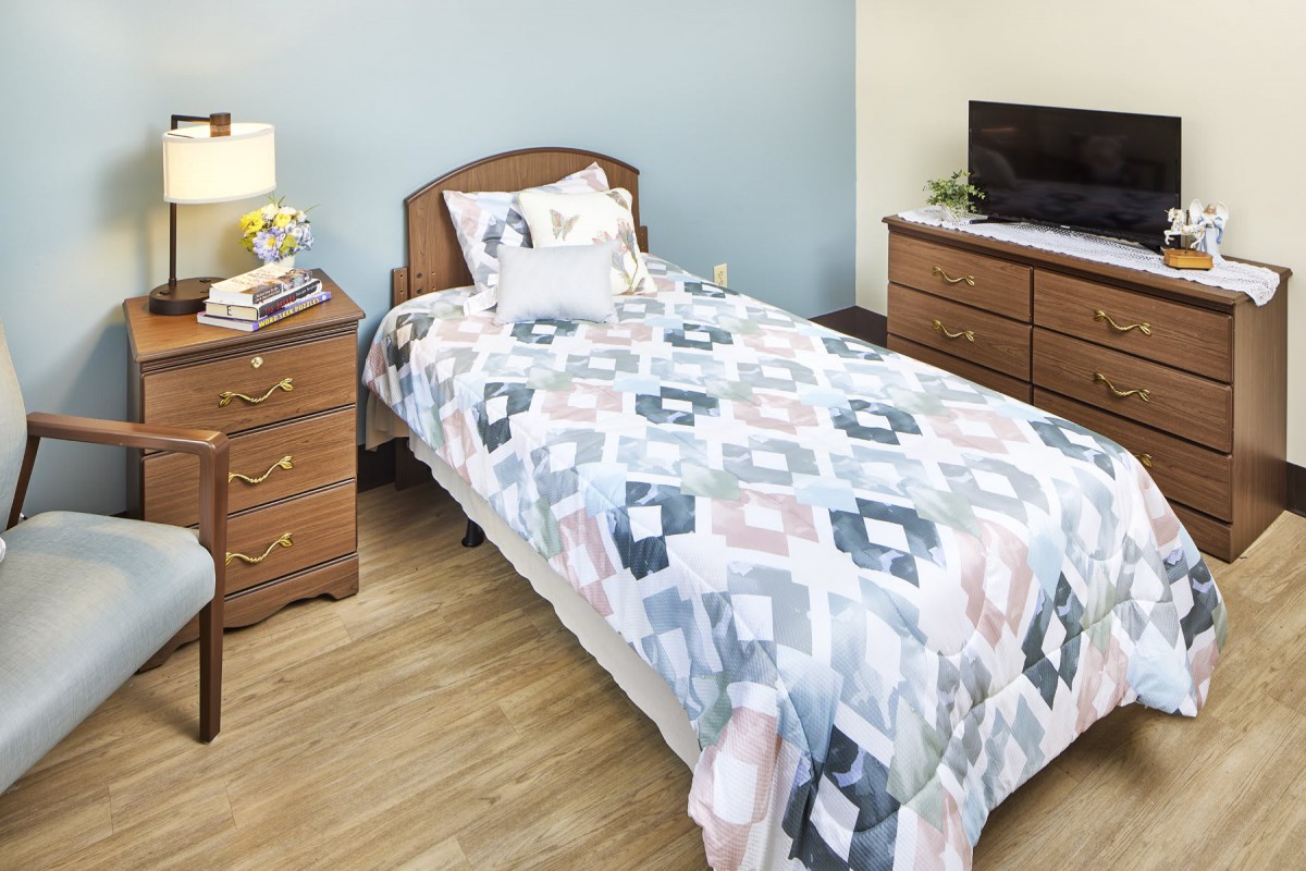 A cozy bedroom with a single bed, wooden furniture, and a patterned quilt.