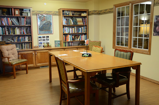 A cozy library meeting room featuring a wooden table, comfortable chairs, and shelves filled with books.