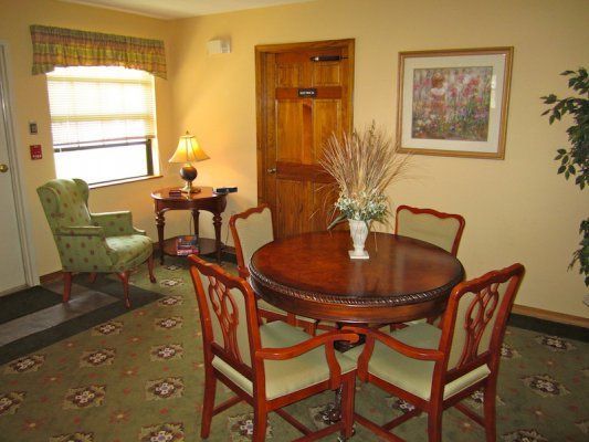 A cozy dining area with a round wooden table, surrounded by four chairs, and a small side table with a lamp.