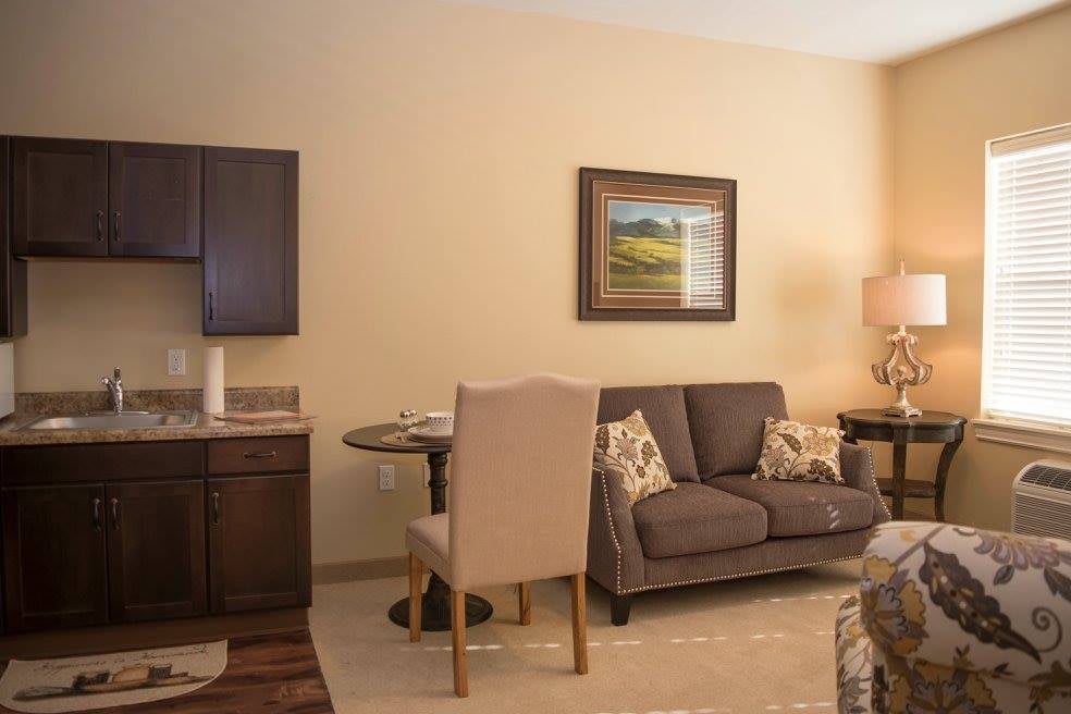 A cozy living room with a sofa, table, and chairs, featuring warm neutral tones and decorative artwork.