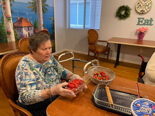 An elderly woman prepares strawberries in a cozy kitchen setting.