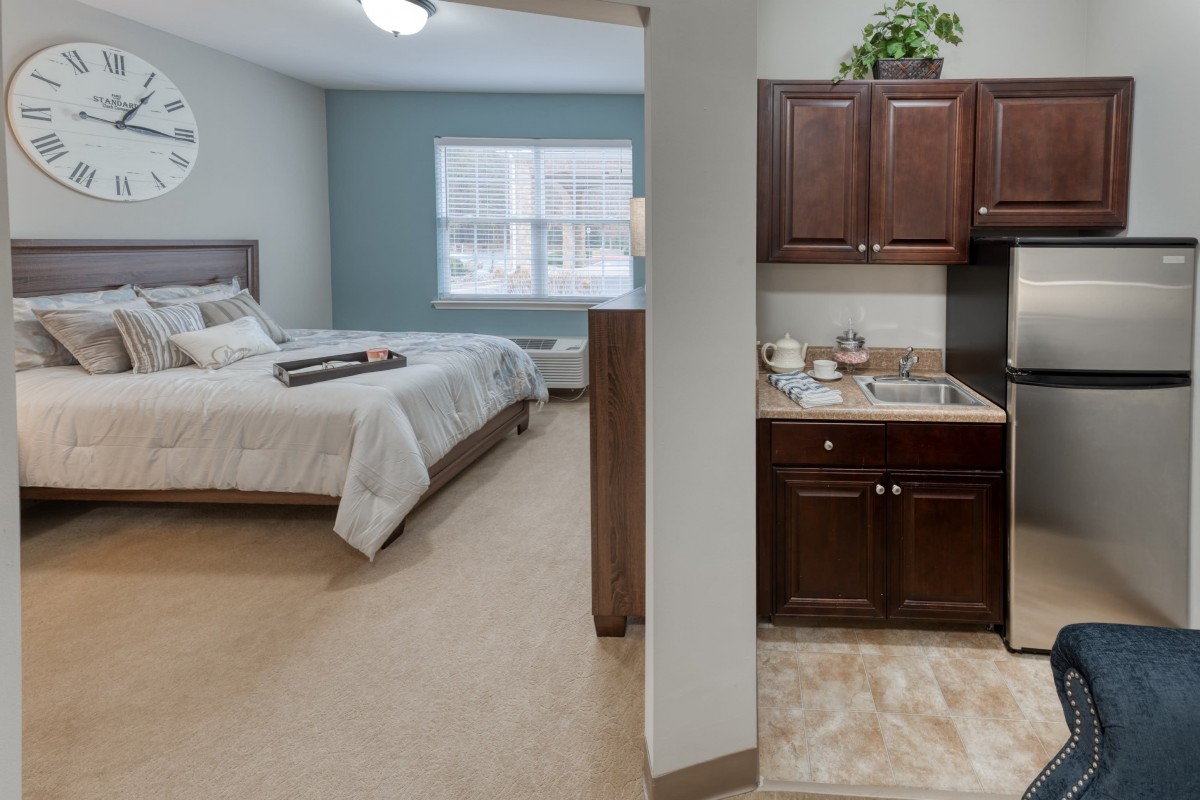 A cozy apartment interior featuring a bedroom with a bed and a small kitchen area.