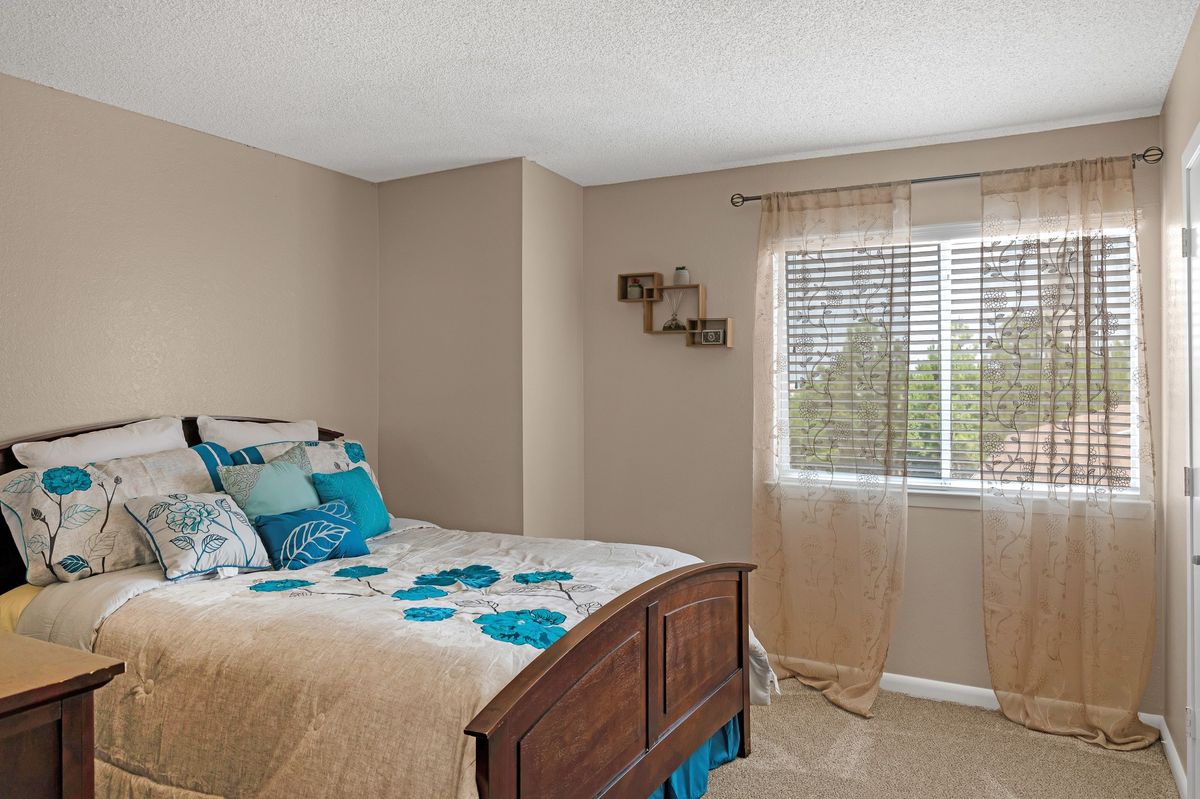 A cozy bedroom with a wooden bed, colorful bedding, and a window with sheer curtains.