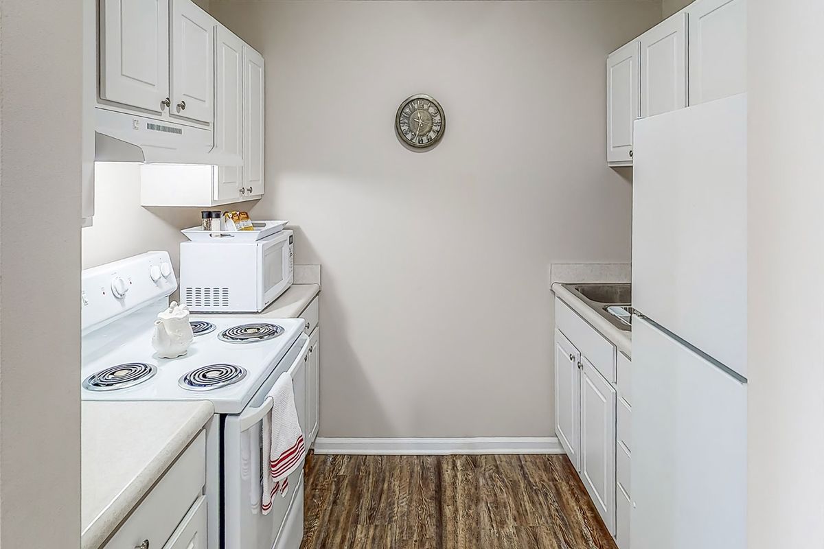 A compact kitchen featuring white appliances and cabinetry with wooden flooring.