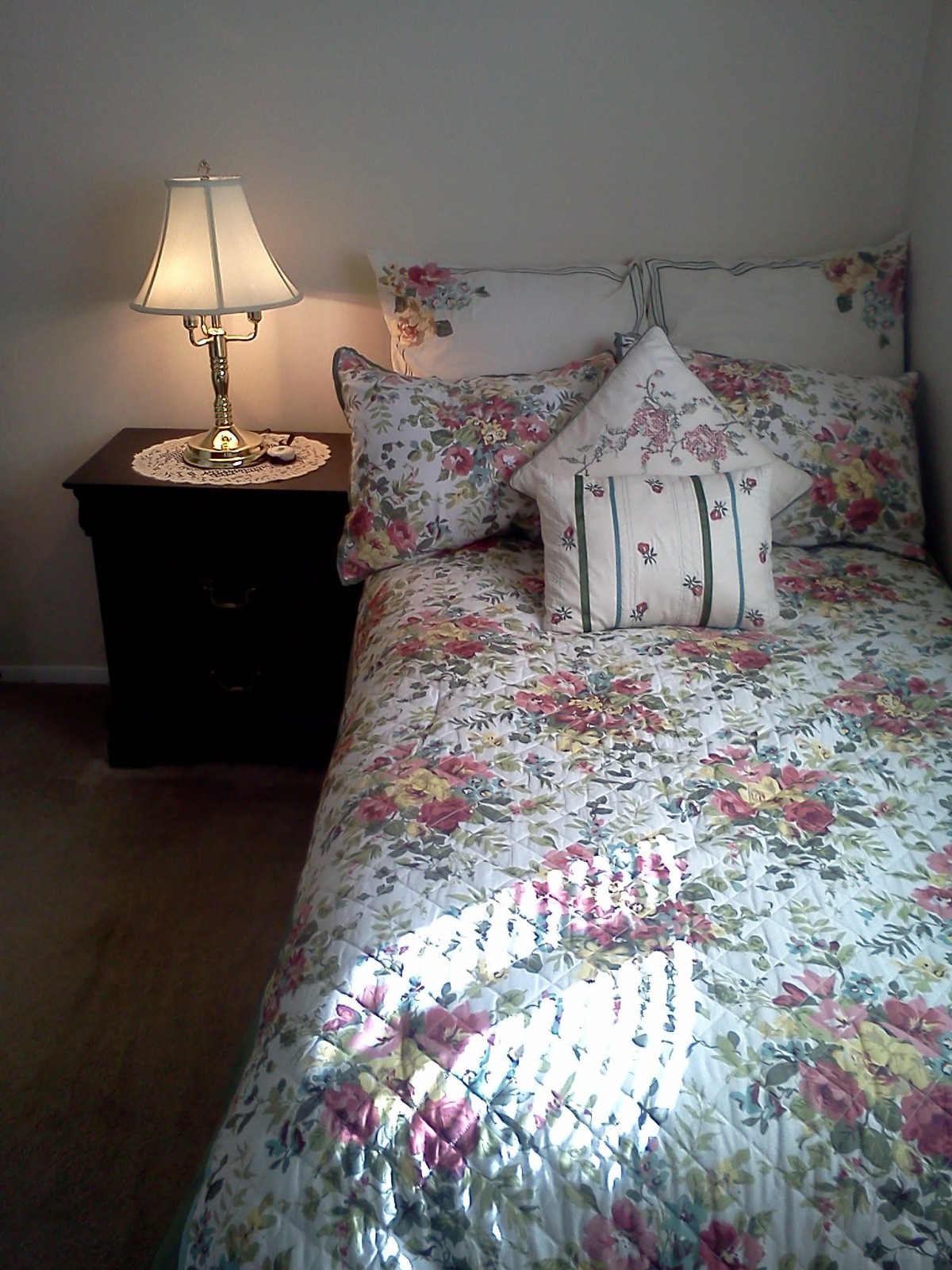 A cozy bedroom with floral bedding and a bedside lamp.