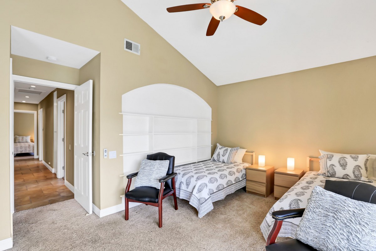 A bedroom featuring two twin beds, neutral walls, a ceiling fan, and carpeted floor.