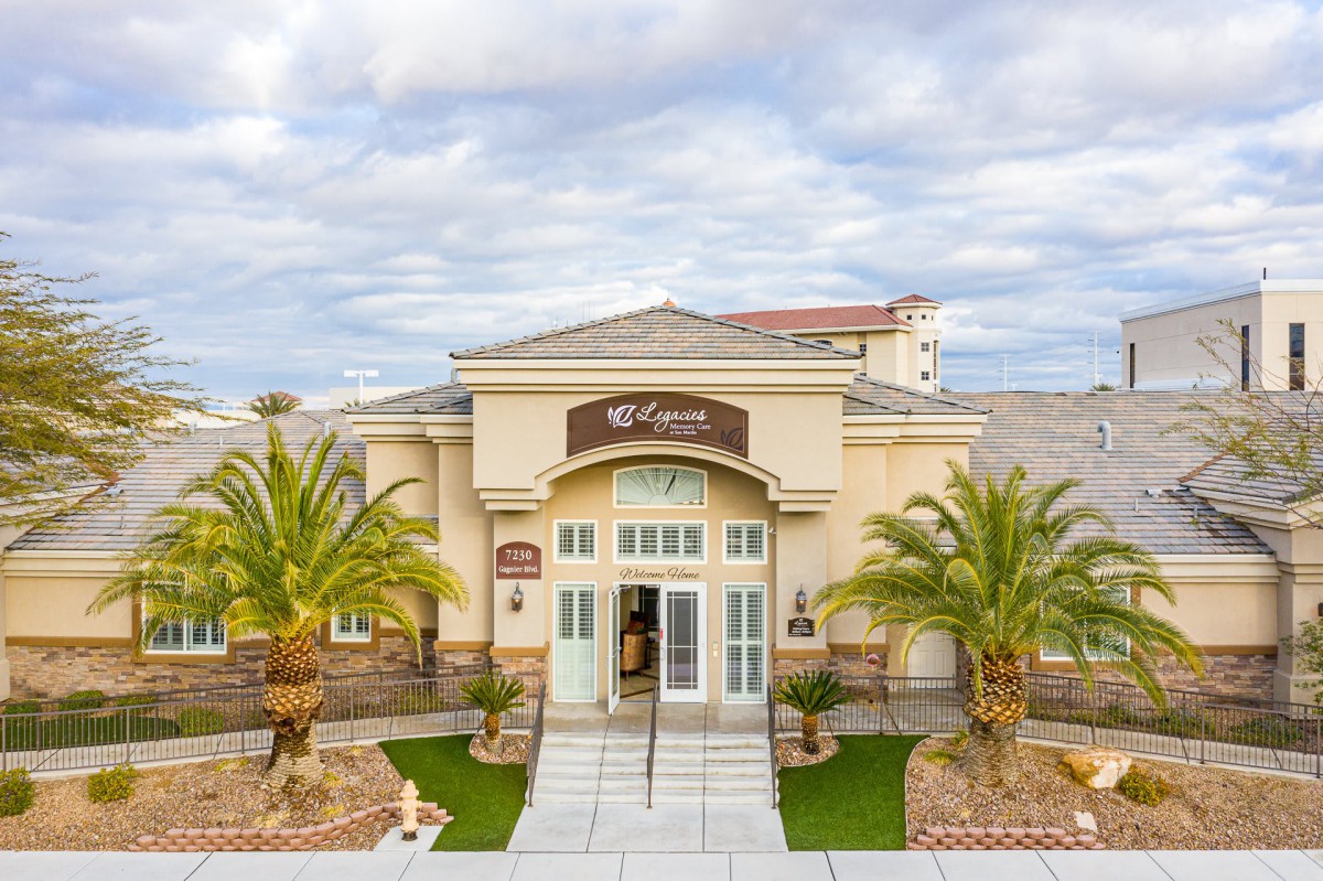 A well-maintained building entrance with palm trees and a cloudy sky backdrop.