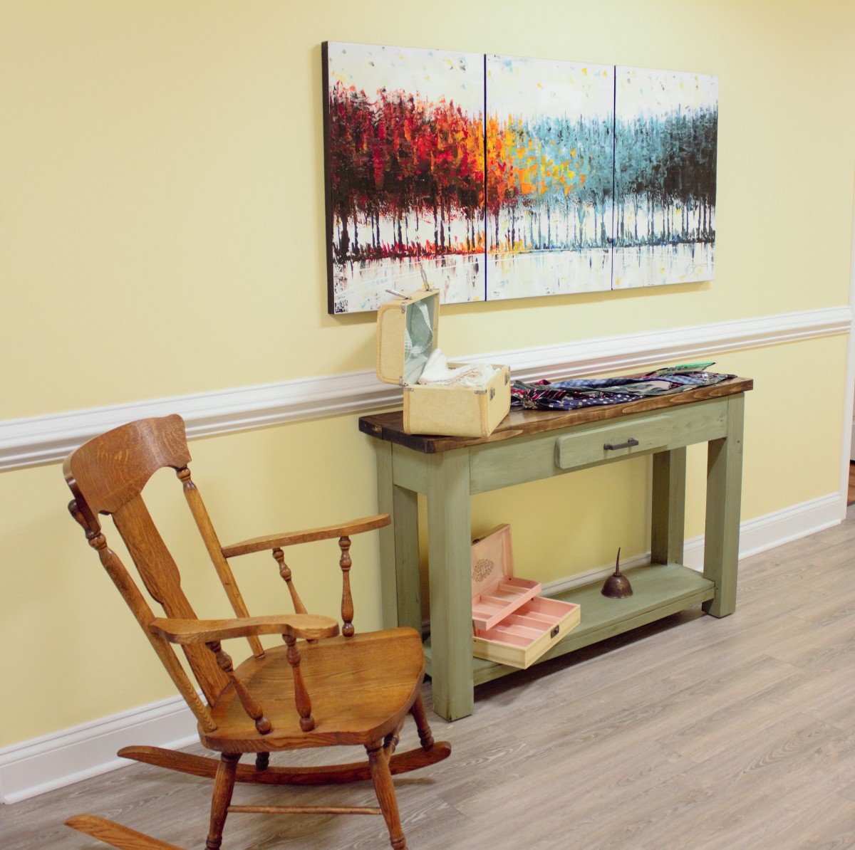 A cozy corner featuring a wooden rocking chair, a console table with a typewriter, and vibrant artwork on the wall.