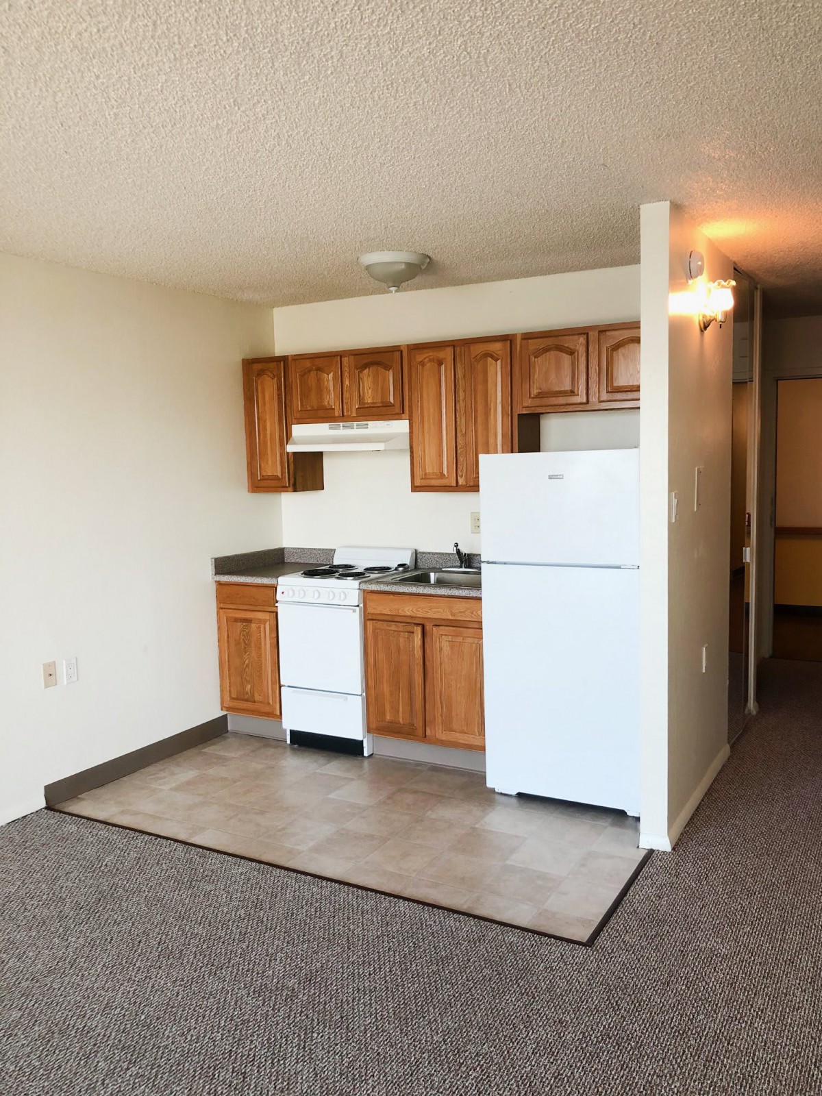 A compact apartment kitchen with wooden cabinets and a white refrigerator.