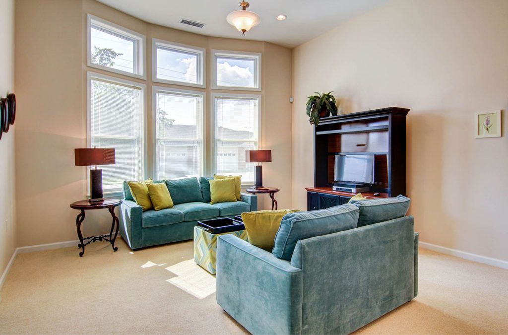 A cozy living room with teal sofas, a TV stand, and large windows allowing plenty of natural light.