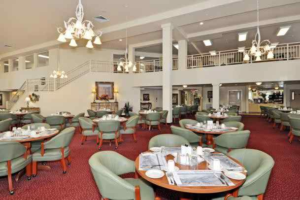 An elegant dining room with neatly arranged tables and chairs, featuring a chandelier and red carpet.