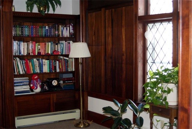 A cozy library nook with a wooden bookshelf filled with books, a floor lamp, and plants by the window.