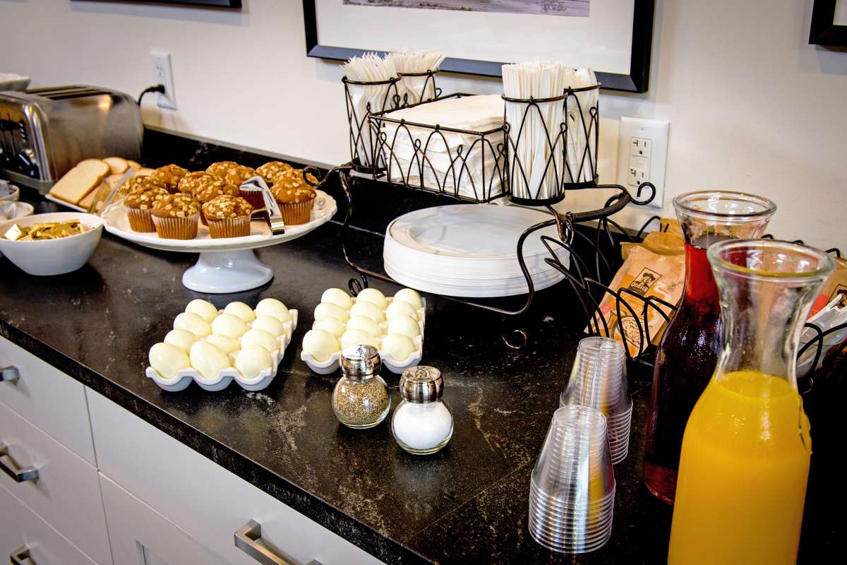 A breakfast buffet with muffins, beverages, and condiments on a countertop.