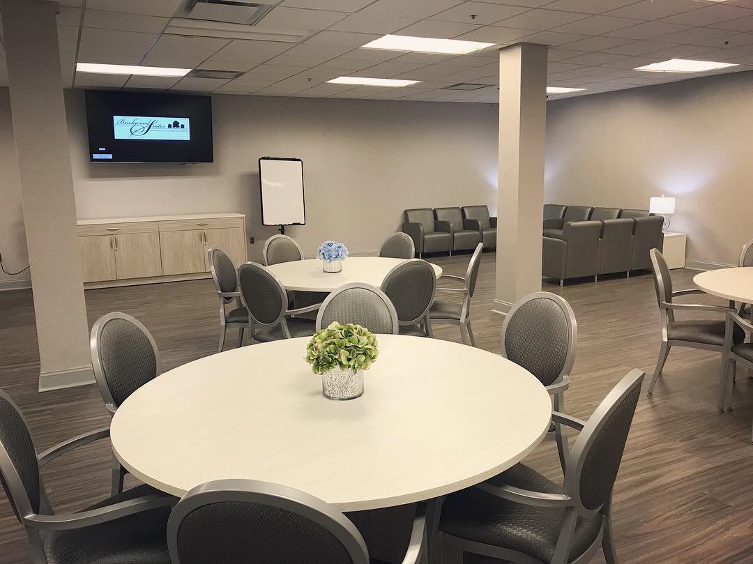 A modern meeting room with round tables, chairs, a television, and a sofa area.