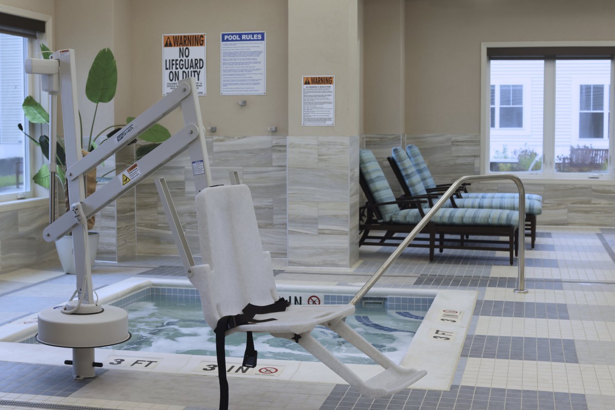 An indoor pool area with a handicap lift and seating.