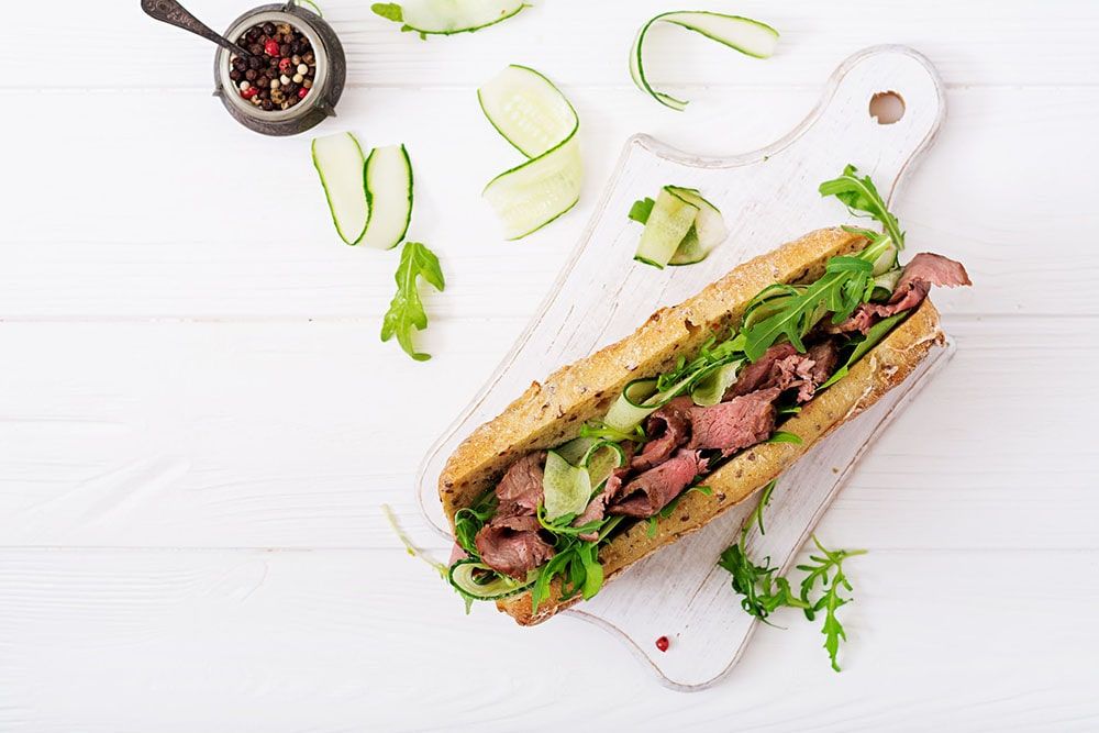 A delicious sandwich filled with meat, fresh greens, and cucumber slices on a wooden board.
